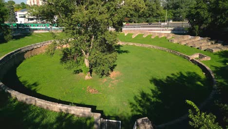 Baum-In-Der-Mitte-Des-Zivilen-Amphitheaters-Von-Aquincum-Mit-Zug-Und-Verkehr-Im-Hintergrund-In-Budapest,-Ungarn