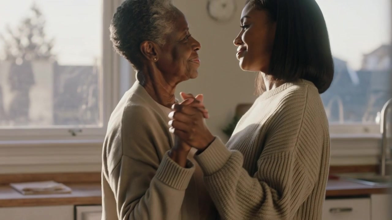 Hugging mom in cardigan and daughter in sweater holding hands swaying in kitchen, bonding with mug