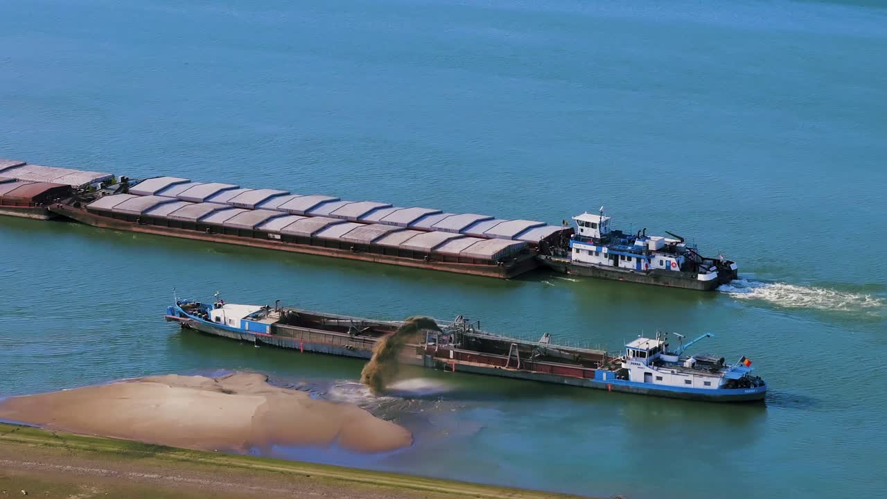 Aerial close up shot of a dredger unloading dredged sand on a big river, other ships passing by, sunny day
