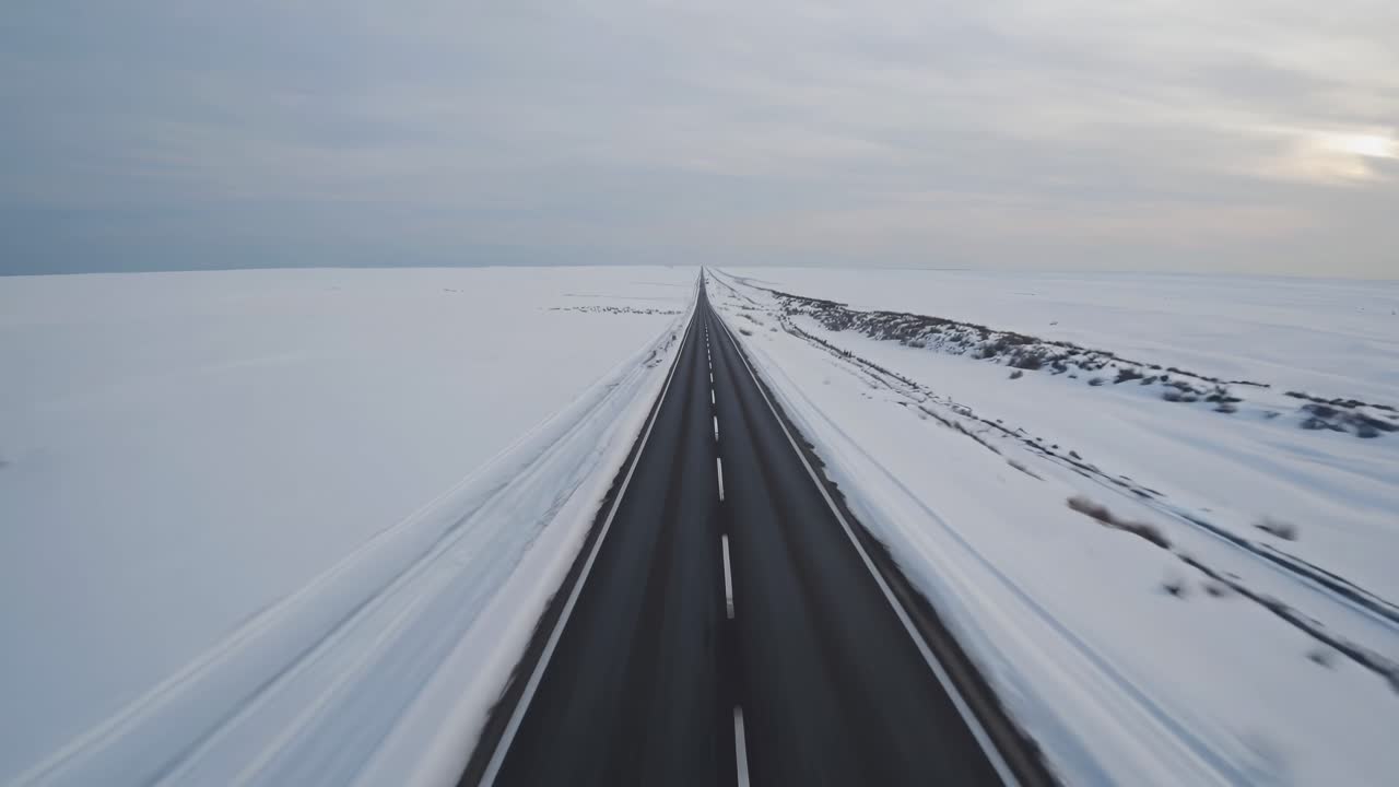 Aerial view of a long, straight road cutting through a vast snowy landscape, creating a serene