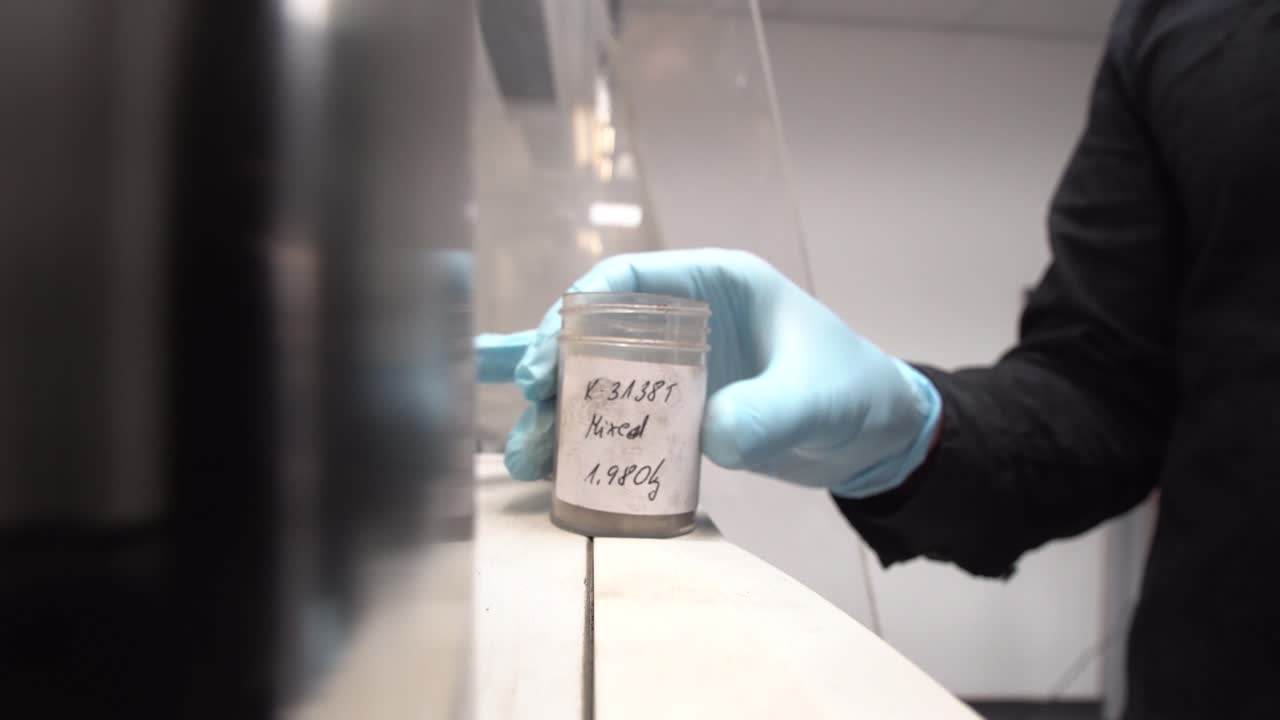 Research lab worker opens sample container lid with grey dry powder in