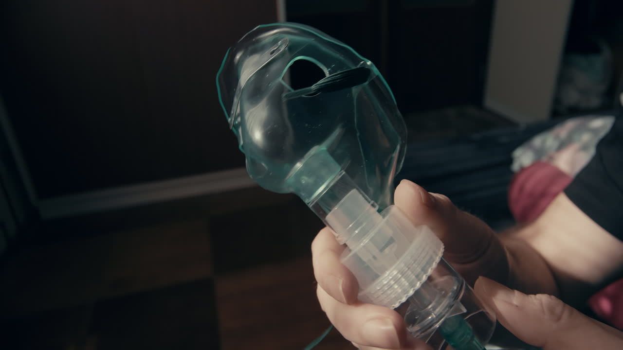 Nærbilde av hender som plasserer en pustemaske over et usett ansikt i hjemlige omgivelser. Egnet for temaer som hjemmesykepleie, respiratorisk støtte og medisinsk assistanse.