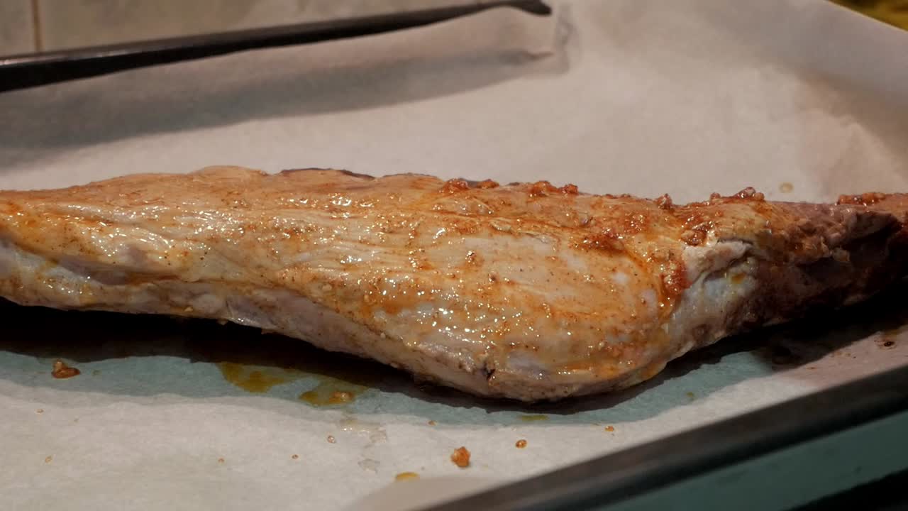 Juicy rack of ribs being brushed with marinade, cooking on a baking sheet