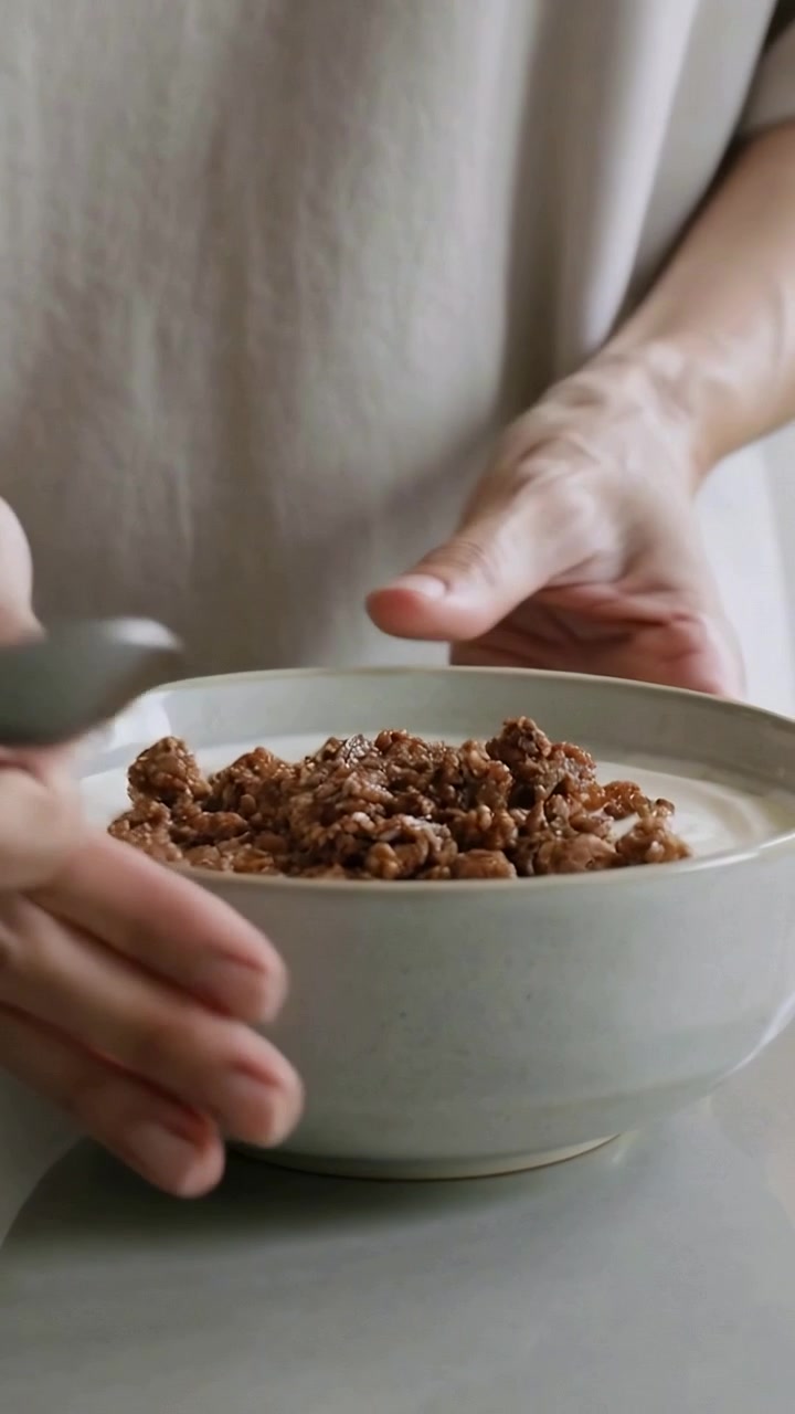 Video verticale: Donna con un top ampio che preme un cucchiaio e sistema la granola sul latte per mostrarla nella ciotola.