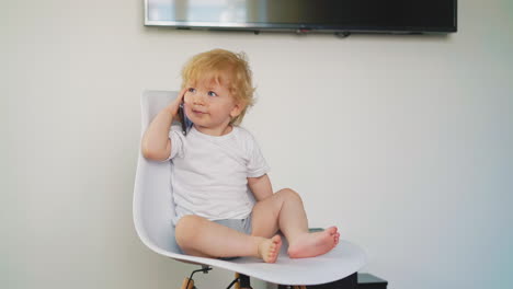 Kleiner-Sohn-In-T-Shirt-Und-Pumphose-Sitzt-Mit-Telefon-Auf-Einem-Stuhl