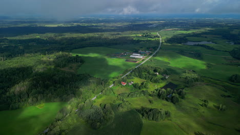 shadow of clouds passing on highway in the middle of lush green fields and forest on a cloudy day