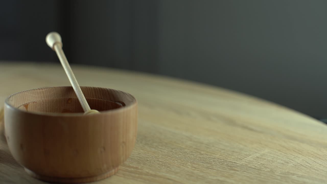 honey in a deep wooden bowl, rustic wooden plate. The wooden spoon drips slowly.