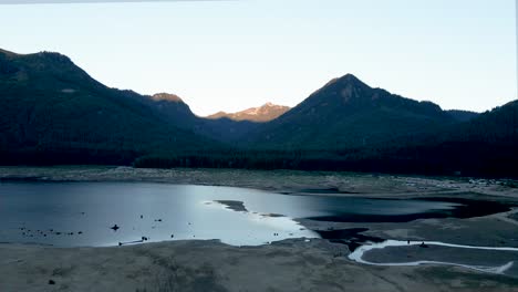 Alpine-light-reflecting-off-a-mountain-top-glacier-fed-lake,-Snoqualmie-Pass,-sunrise-aerial