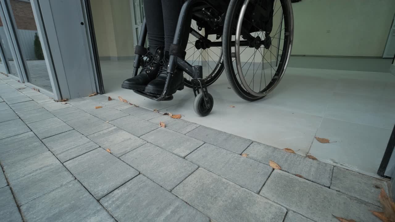Disabled woman in wheelchair at home comes out to modern office building