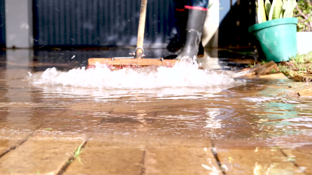 Man wearing black boots sweeps standing water from driveway after heavy rainfall