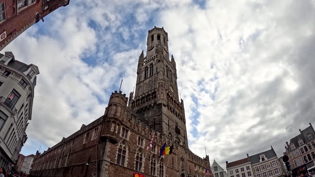 Wide-angle upward view of Bruges belfry tower with circling seagulls and dramatic cloudy sky