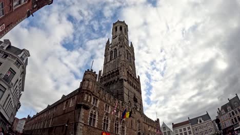 Wide-angle upward view of Bruges belfry tower with circling seagulls and dramatic cloudy sky