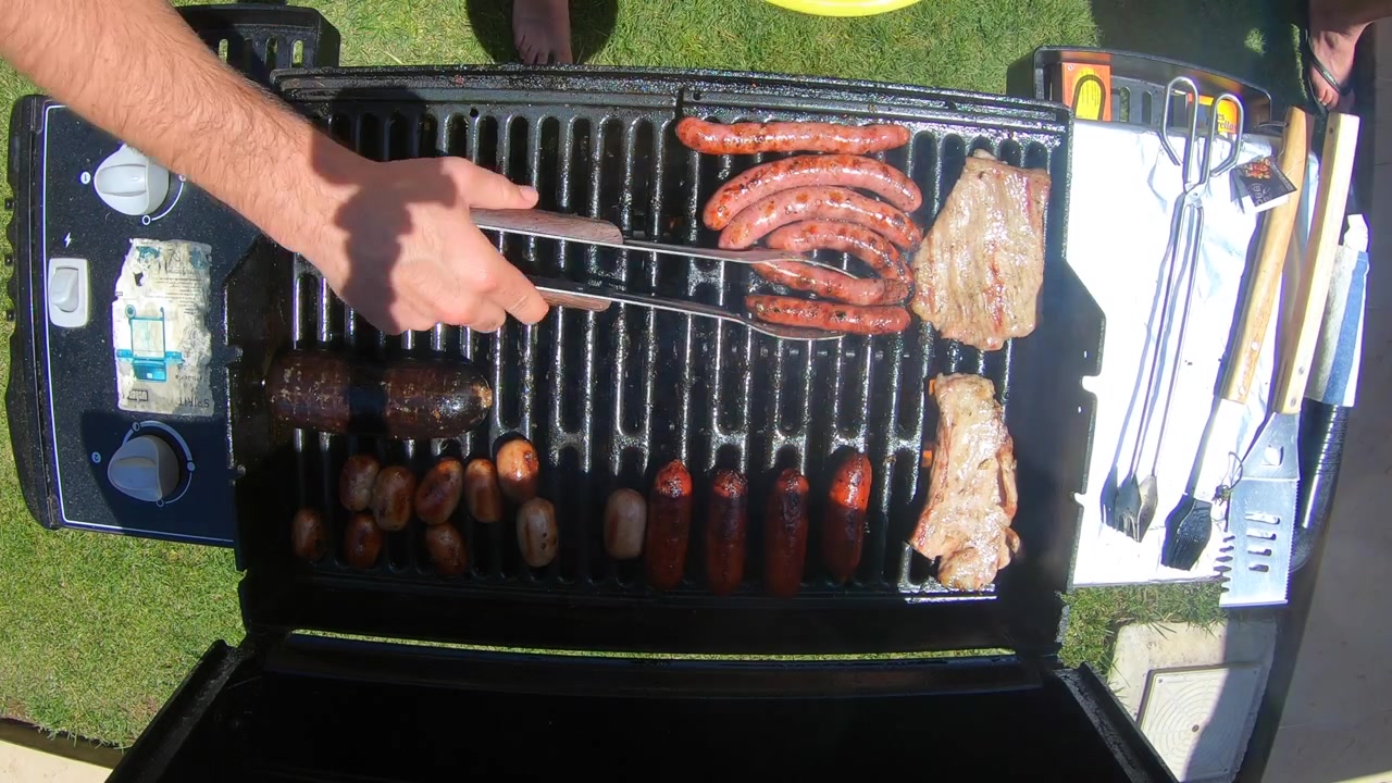 Filmato dall'alto di asparagi, bistecche e salsicce che cuociono su una griglia per barbecue all'aperto. Scena di grigliata estiva in giardino con verdure sane e carne preparate a fuoco vivo su un barbecue a gas