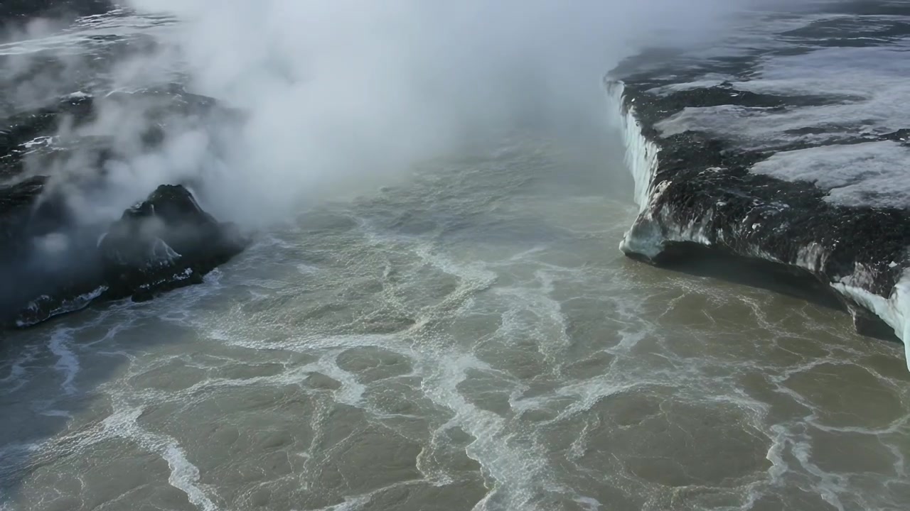 Fluxo de rio aéreo empurrando água sobre o penhasco, formando cachoeira em queda livre, poça turbulenta, névoa subindo.