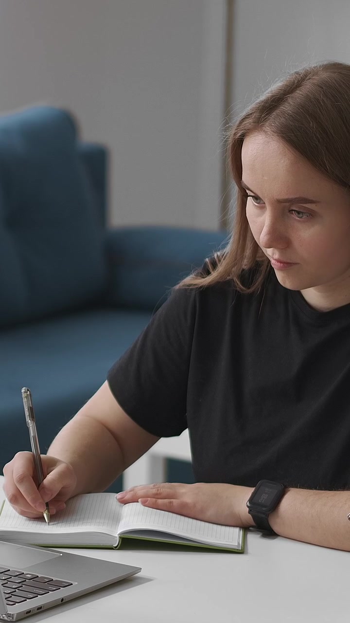 Ung kvinne skriver i notatbok mens hun studerer hjemme