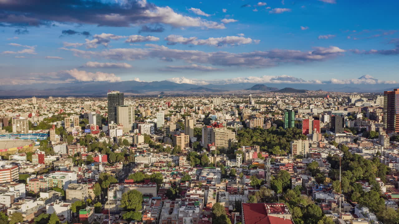 Mexico City'de çok açık bir öğleden sonra, Azul stadyumu, Meksika Boğa Güreşi Arenası, bazı gökdelenler, Hundido parkı ve arkada karlı volkanların olduğu havadan hyperlapse çekimi.