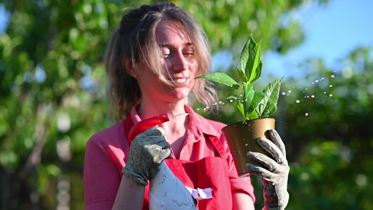 Joyful woman gardener spraying water on a green houseplant in sunlight
