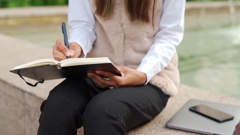 Anonymous-Hispanic-woman-taking-notes-near-fountain