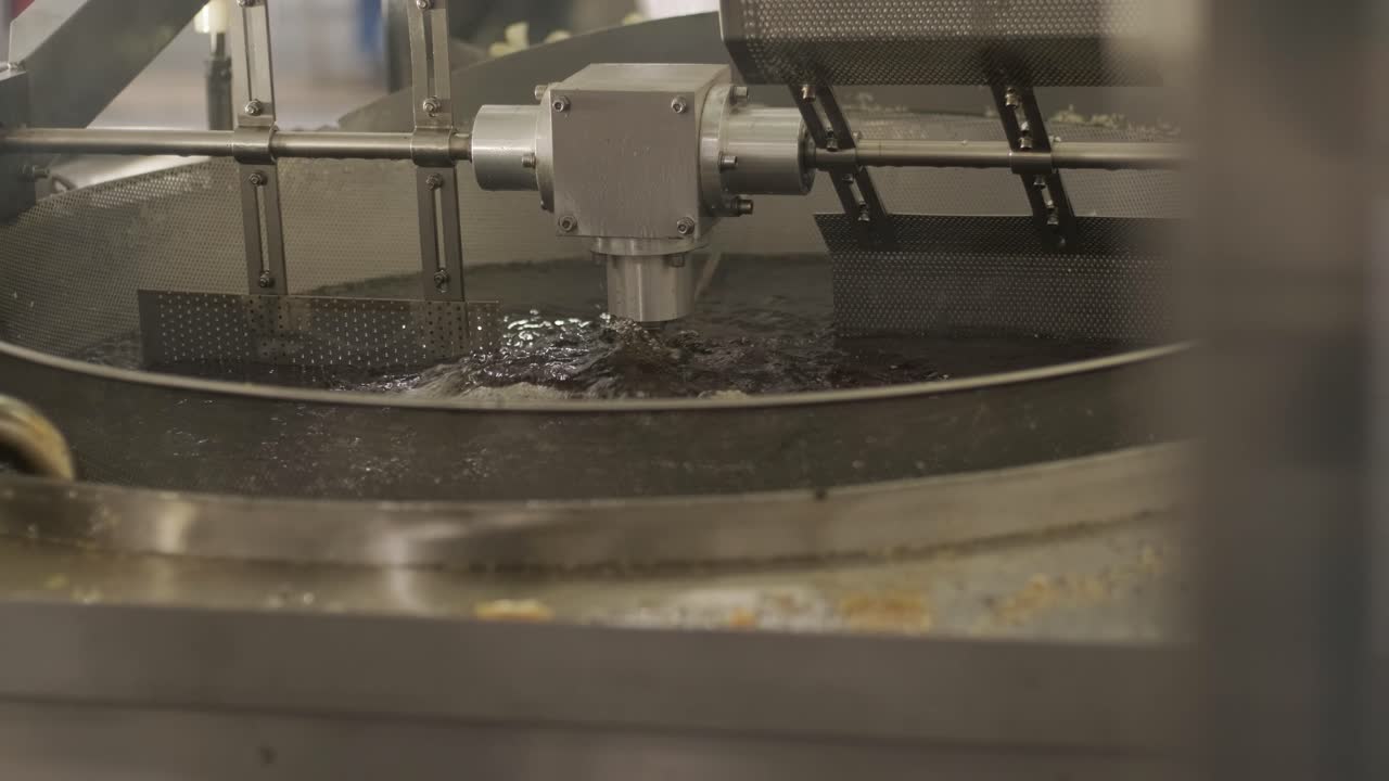 producción de papas fritas y bocadillos. máquina industrial de fritura profunda. las papas fritas se fríen en un cuenco grande con aceite. la línea de producción de la fábrica mueve las papas frias doradas después de freír.