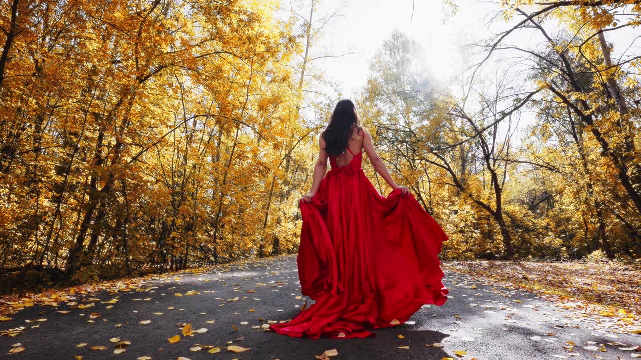 A Captivating Journey Through Autumn: A Woman in a Flowing Red Dress Strolling Along a Sunlit Pathway Surrounded by Golden Leaves, Embracing Nature's Beauty