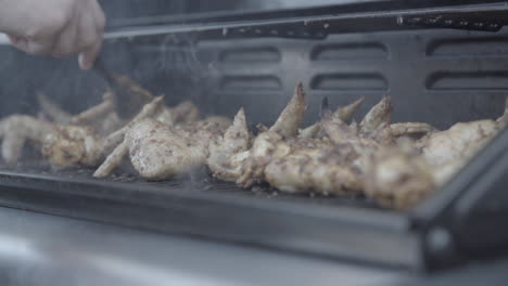 grilling and flipping some chicken wings on the barbecue in slowmotion with some smoke around the meat log