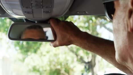 hombre mayor ajustando el espejo trasero del coche