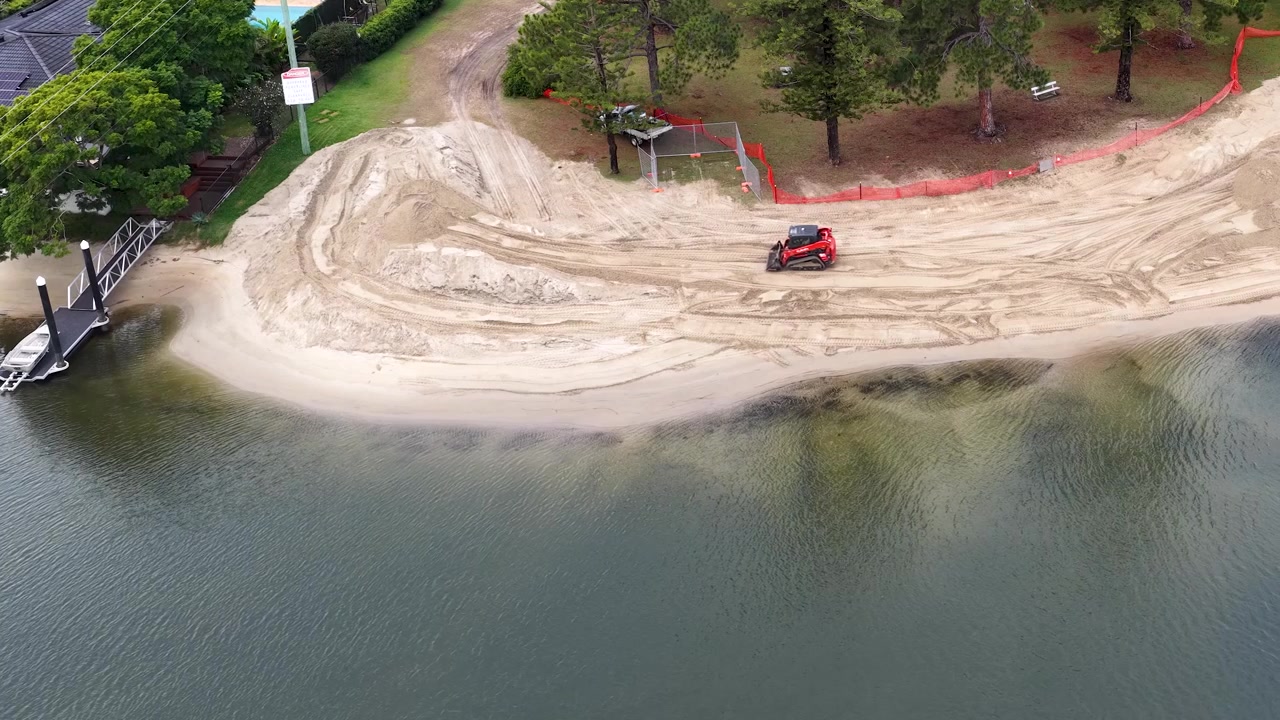 Ripresa aerea con drone di macchinari pesanti che spostano sabbia durante il ripristino della spiaggia di una proprietà sul lungomare.