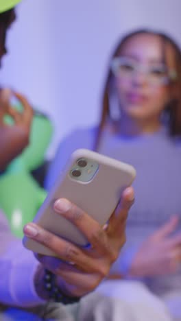 close up vertical video studio shot of young gen z friends sitting on sofa sharing social media post on mobile phones