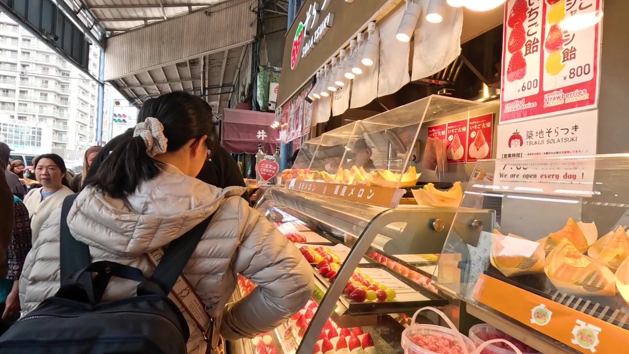 ダウンジャケットを着た女性が、東京の築地場外市場でいちご串を見る