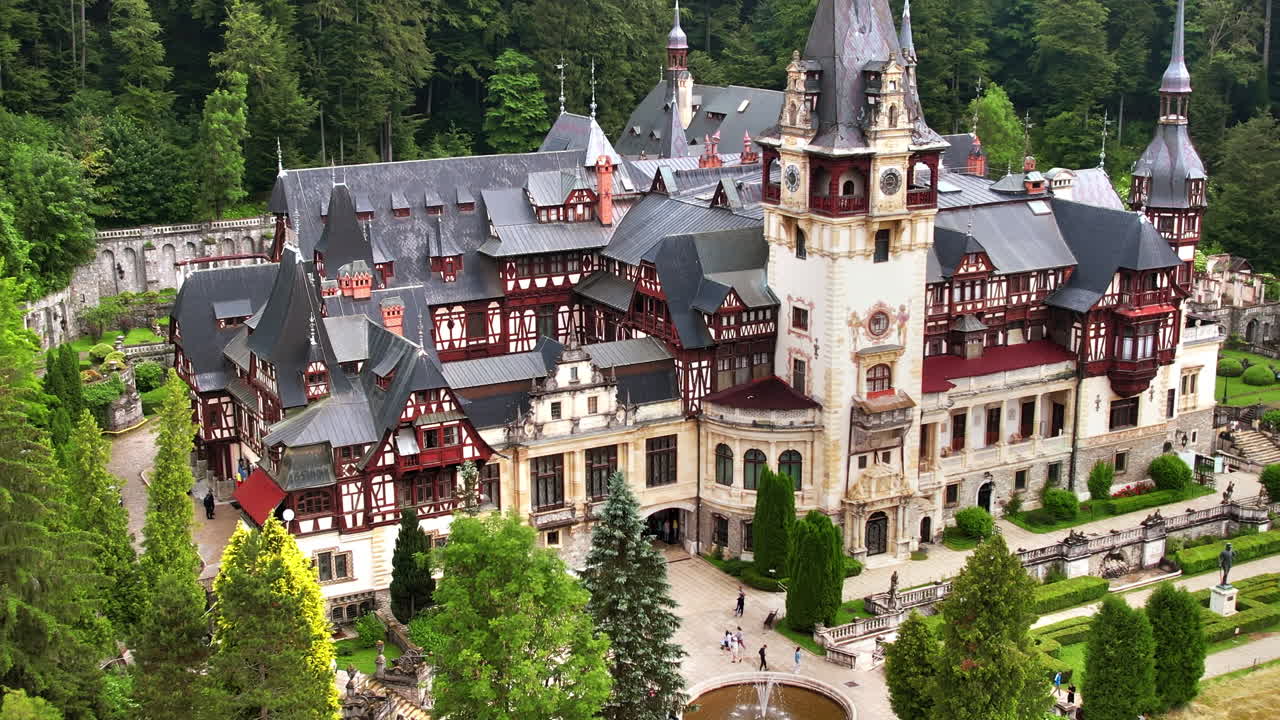Aerial drone view of The Peles Castle in Romania. Castle with gardens and tourists in Carpathians, lush forest around it