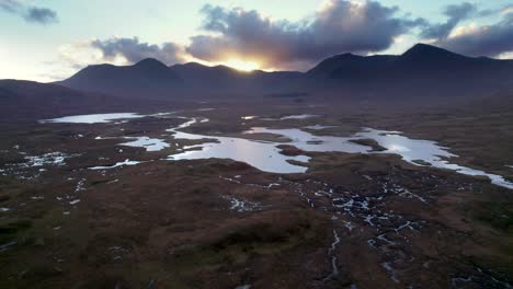 un dron se invierte en lo alto de un paisaje de turberas de turberas entre un mosaico de lagos de agua dulce que miran hacia las montañas oscuras en el horizonte al atardecer
