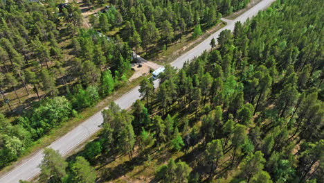 Aerial-view-circling-a-RV-driving-on-a-boreal-forest-road,-summer-day-in-Lapland