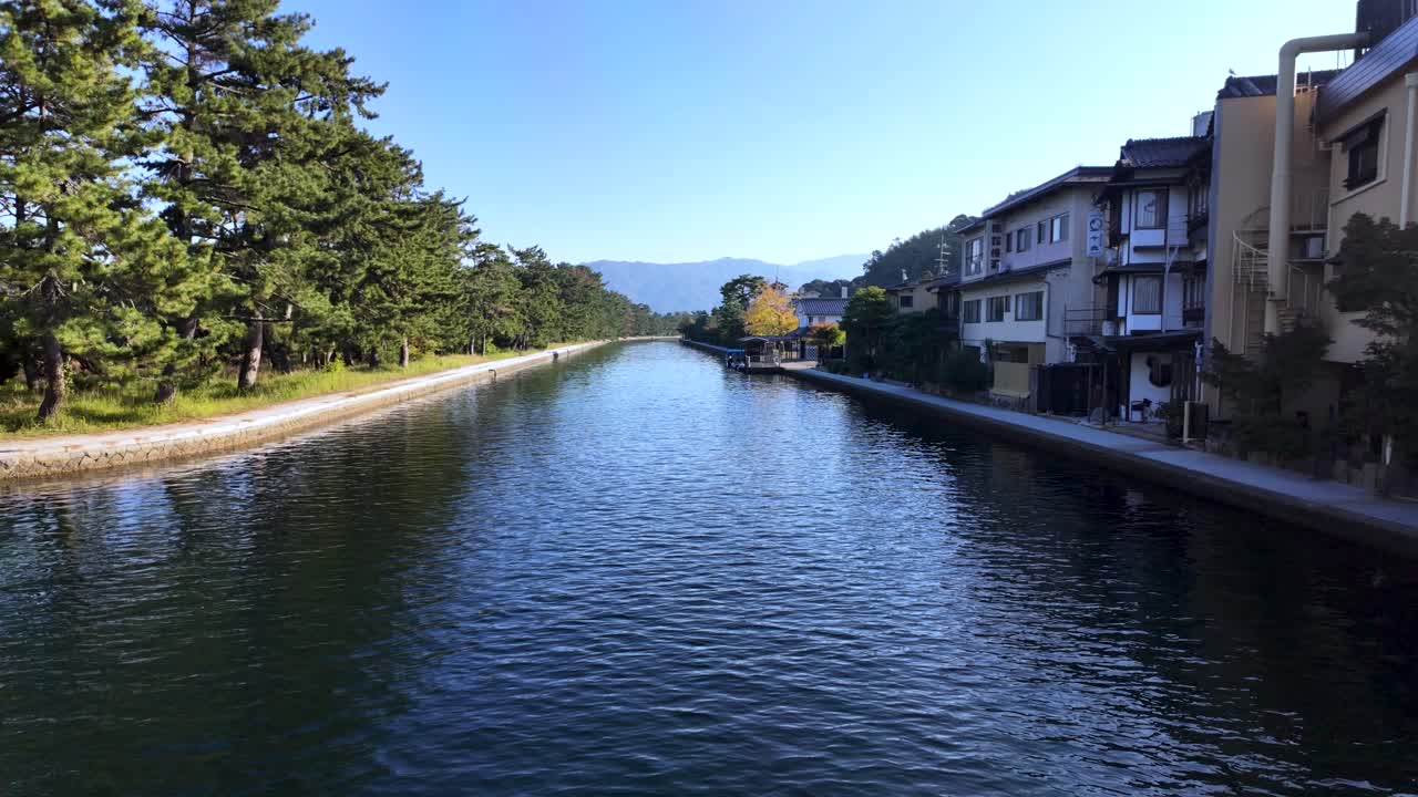 Calm water flowing in the canal between pine trees and houses in Amanohashidate, Japan, during a sunny day