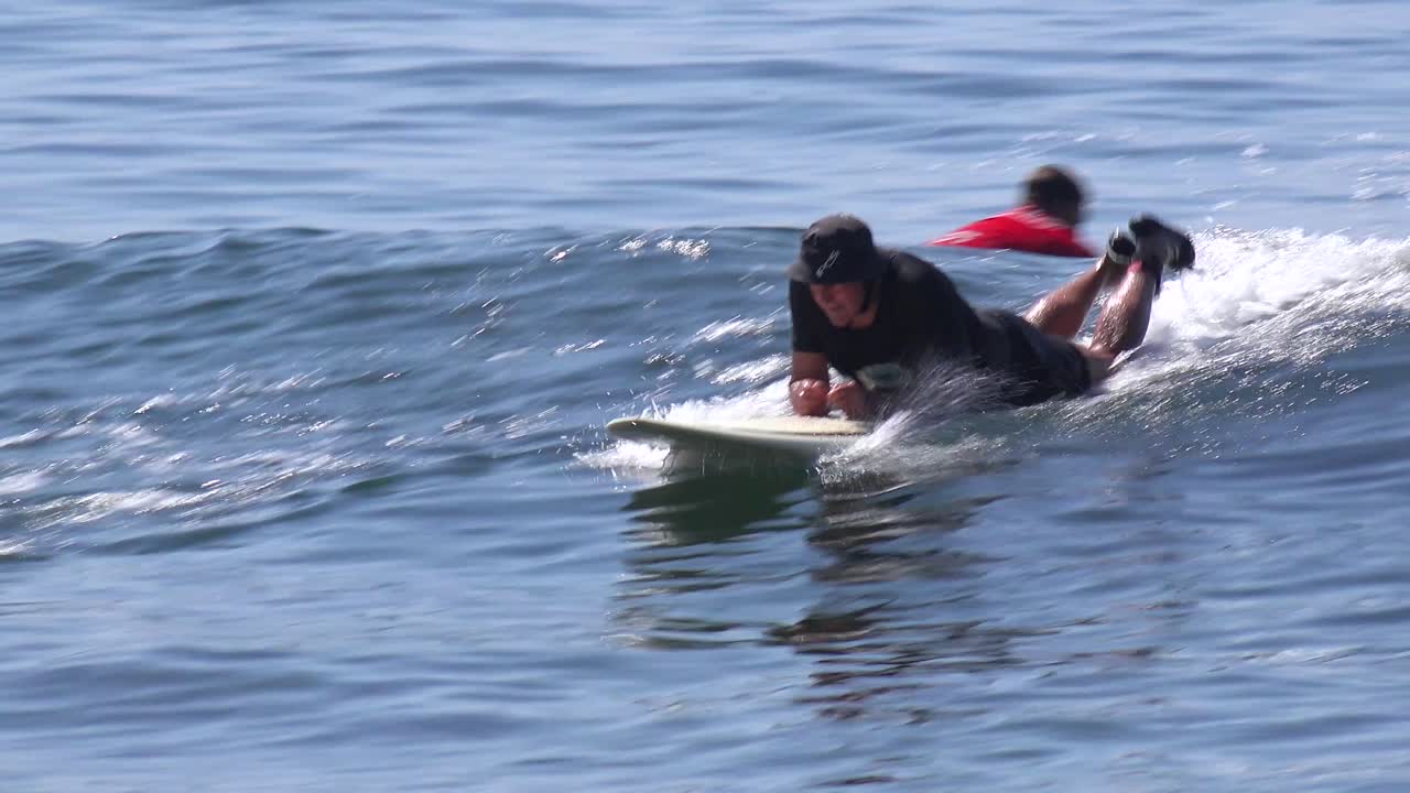 un surfista de mediana edad hace bodyboard en una ola en una playa del sur de california