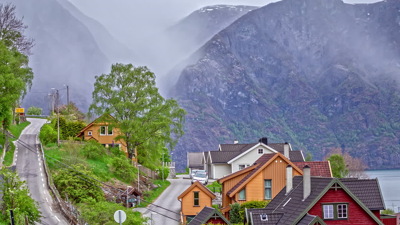 amplio tiro de niebla que pasa sobre casas escénicas en la ladera de la montaña con carretera sinuosa