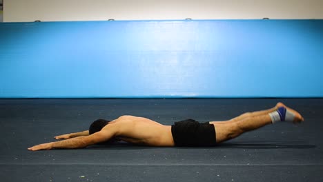 a guy doing an abs workout in a gymnastics gym doing lying down shortless leg and hand raises still shot