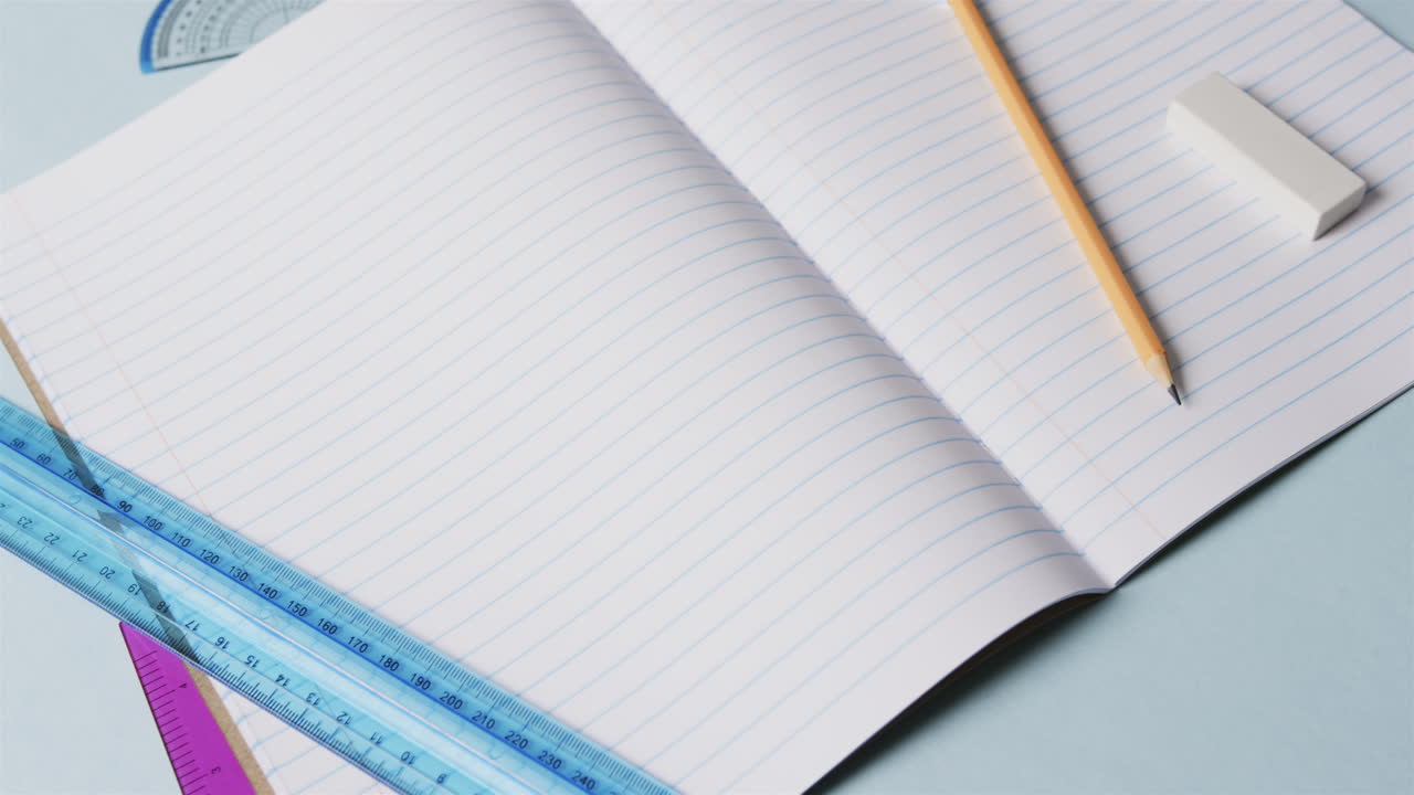 Close up of open notebook with school stationery on blue background, in slow motion