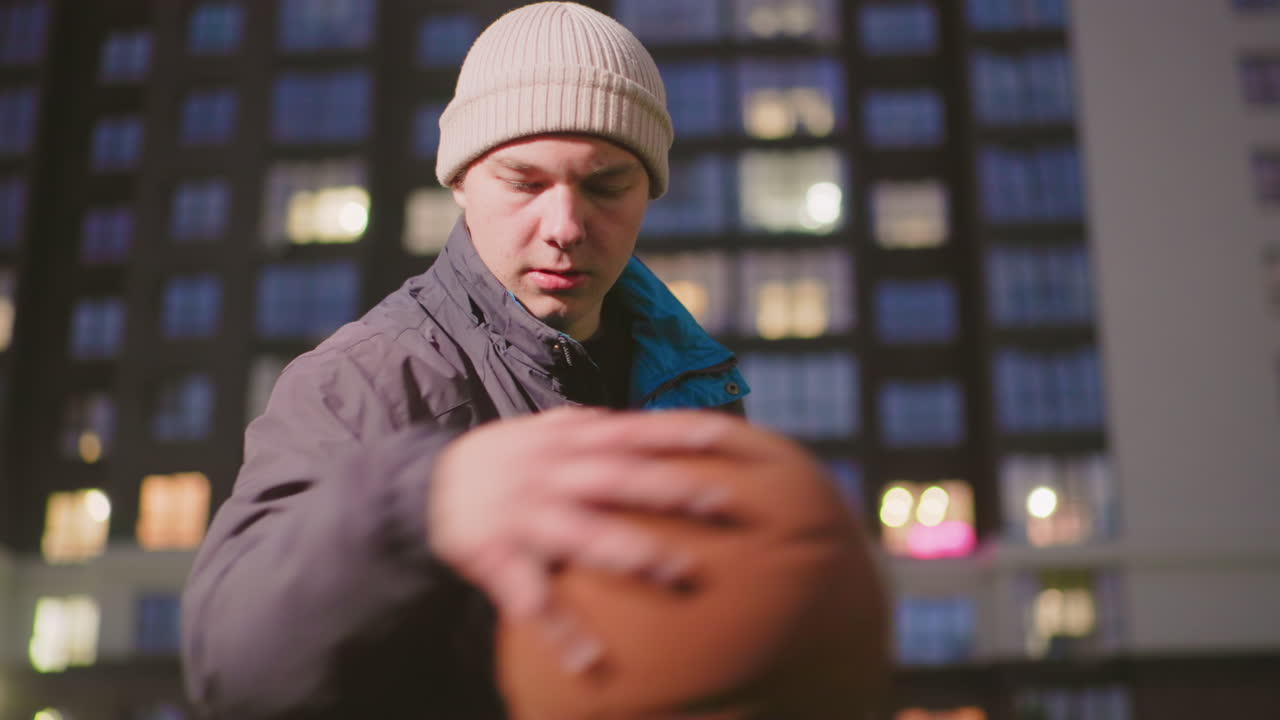 night rooftop cityscape showing solitary man in beanie and coat, walking along balcony railing under soft bokeh lights from highrise windows, cinematic bluehour mood, pensive expression, cold