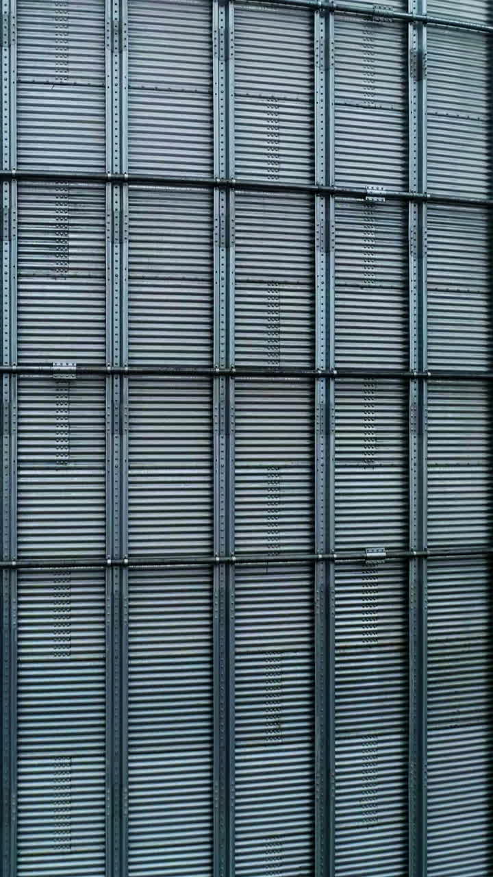 Metal surface of huge elevator container. Rising along the silver shell of granary tank up to the top. Foggy sky backdrop. Vertical video