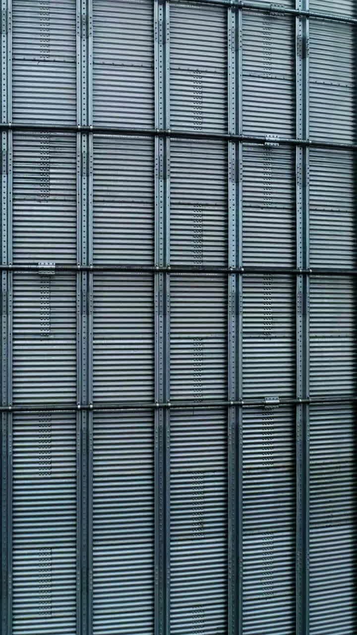 Metal surface of huge elevator container. Rising along the silver shell of granary tank up to the top. Foggy sky backdrop. Vertical video