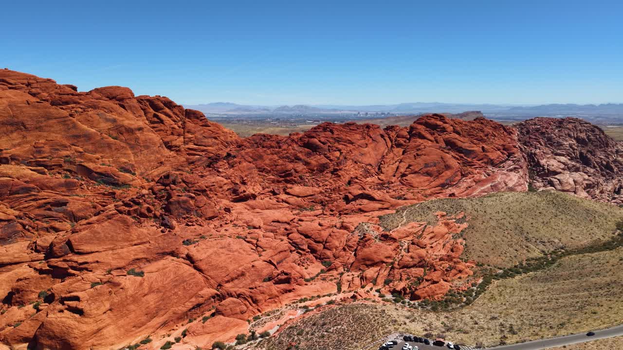 A high-altitude drone shot of the famous 13-mile scenic drive in Red Rock Canyon, showcasing the massive red rock formations and a visitor parking area