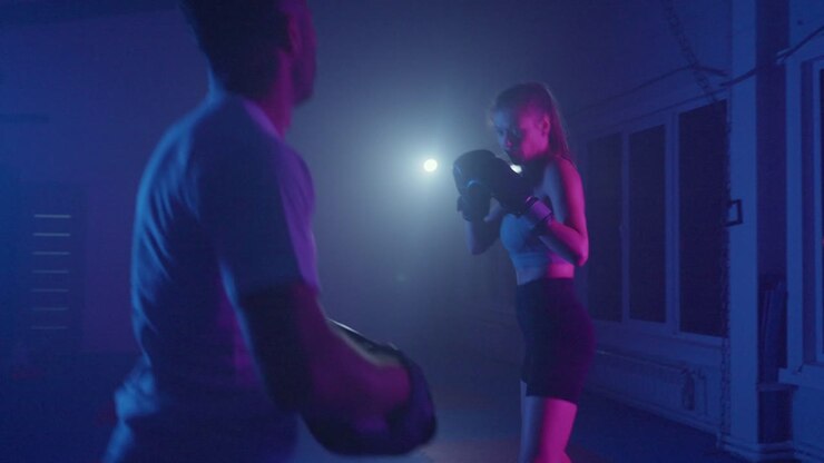 Mujer entrenando kickboxing con entrenador en gimnasio oscuro iluminado con neón