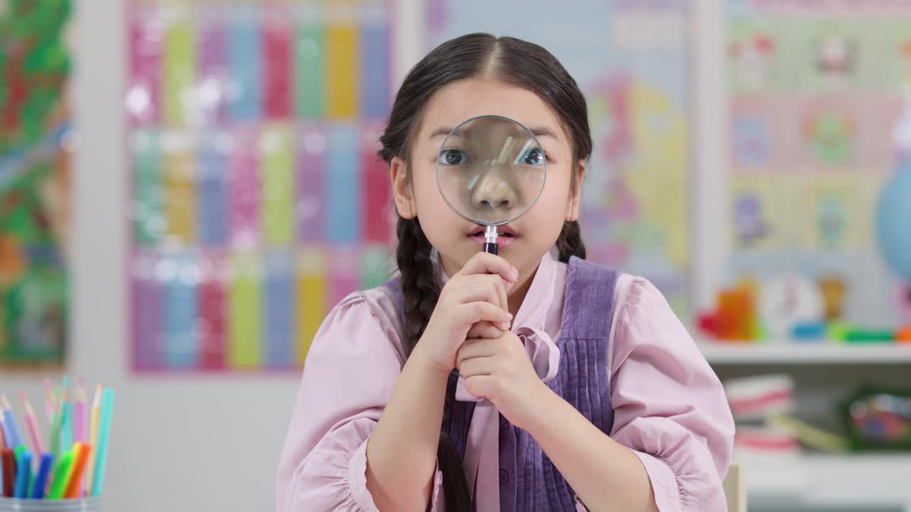 Young girl with braids uses magnifying glass at desk in brightly lit classroom setting