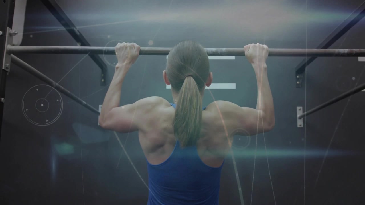 Kvindelig atlet laver pull-ups fra død hæng under træning, med lysreflekser der fremhæver ryggen.