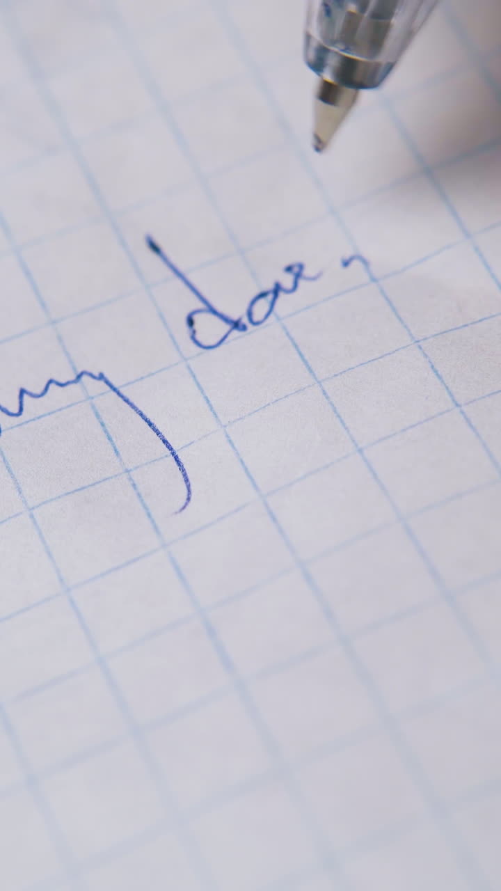 young person writes letter to daddy with blue pen on blank checkered paper sheet extreme close view