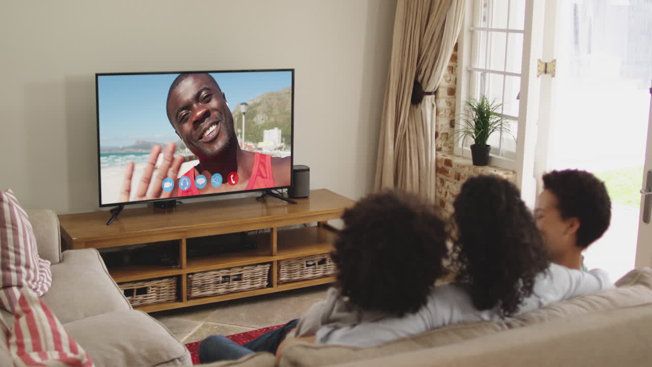 Famiglia afroamericana seduta sul divano che fa una videochiamata con un amico sullo schermo della TV.