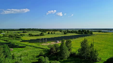 Aerial-view-of-a-solar-panel-field-surrounded-by-grass-and-trees-with-a-river-on-the-background