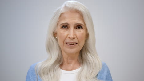 relaxed old woman looking camera indoors. happy lady raising hand in studio.