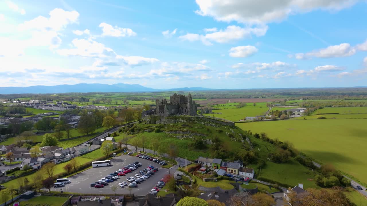 4K Aerial view of the Rock of Cashel, capturing ancient stone walls, round towers, and cathedral ruins surrounded by rolling green fields and historic farmland. Co.Tipperary, Ireland_07