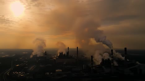 industrial complex at dusk: capturing the contrast of smoke and sunlight over an expansive manufacturing facility in a stunning aerial view